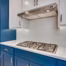 White quartz countertop with a smooth matte finish beneath a gas cooktop, subway tile backsplash, and blue shaker cabinets.